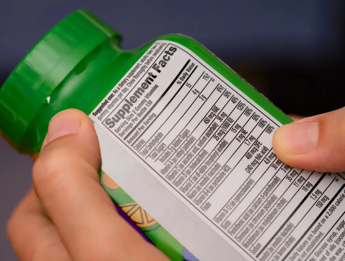 Vegan supplement marketing agency: a close-up shot of a vitamin supplement jar with a supplement facts label at the back in woman hands.