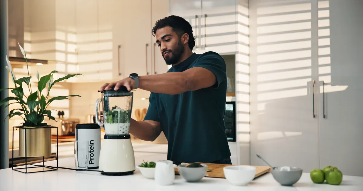 Weight management marketing agency: protein shake, kitchen and man in home for nutrition, breakfast and snack or diet. Blender, bodybuilder and male person with organic ingredients for health, wellness or morning fruit drink in house.