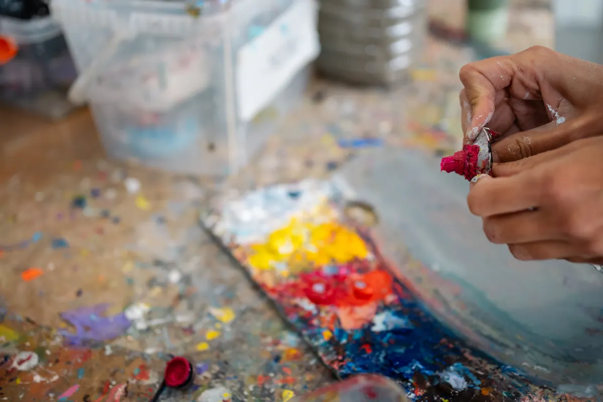 Art supply marketing agency: artist squeezing paint tube on wood table in art studio.