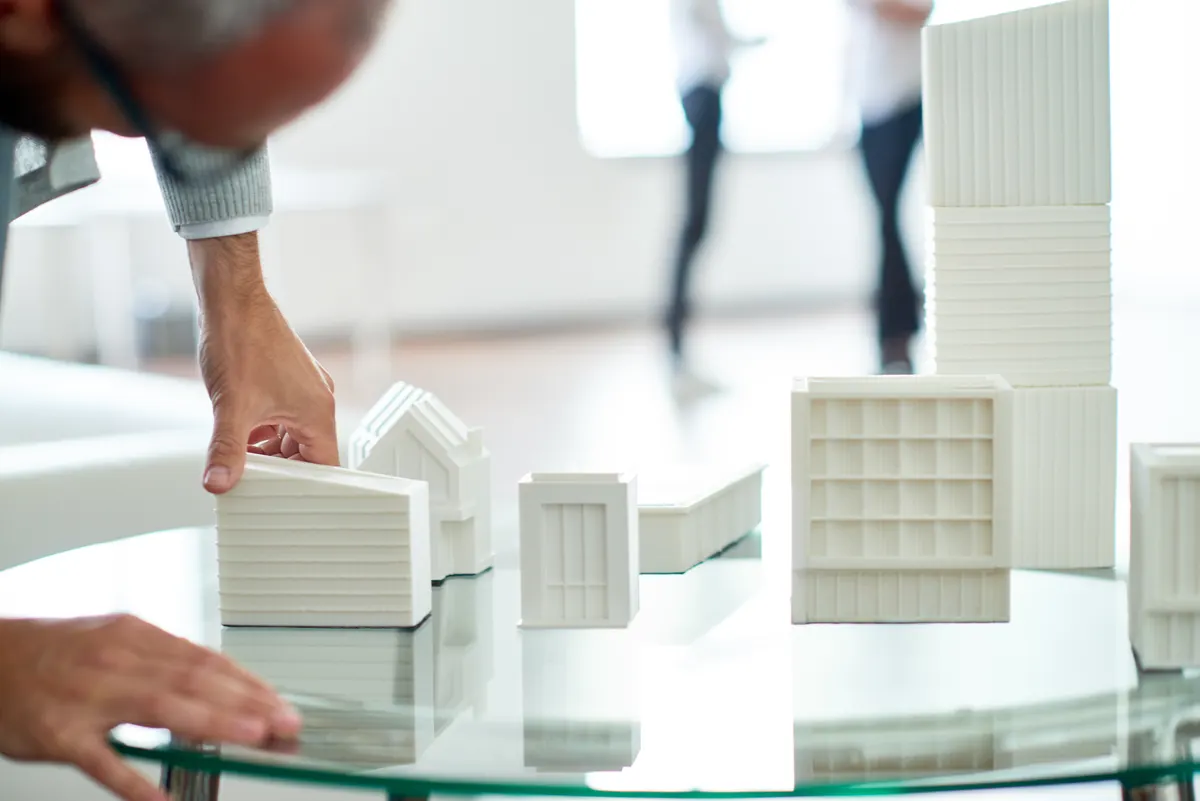 Brick & building set marketing agency: crop man working on three-dimensional building miniature.