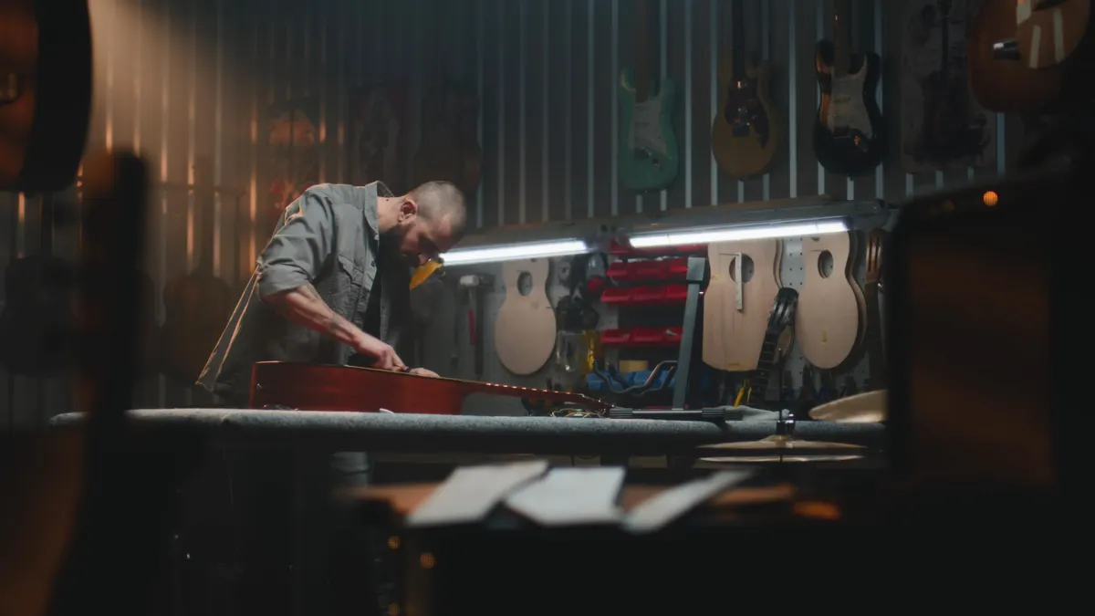 Musical instrument marketing agency: professional male carpenter wipes acoustic guitar with rag.