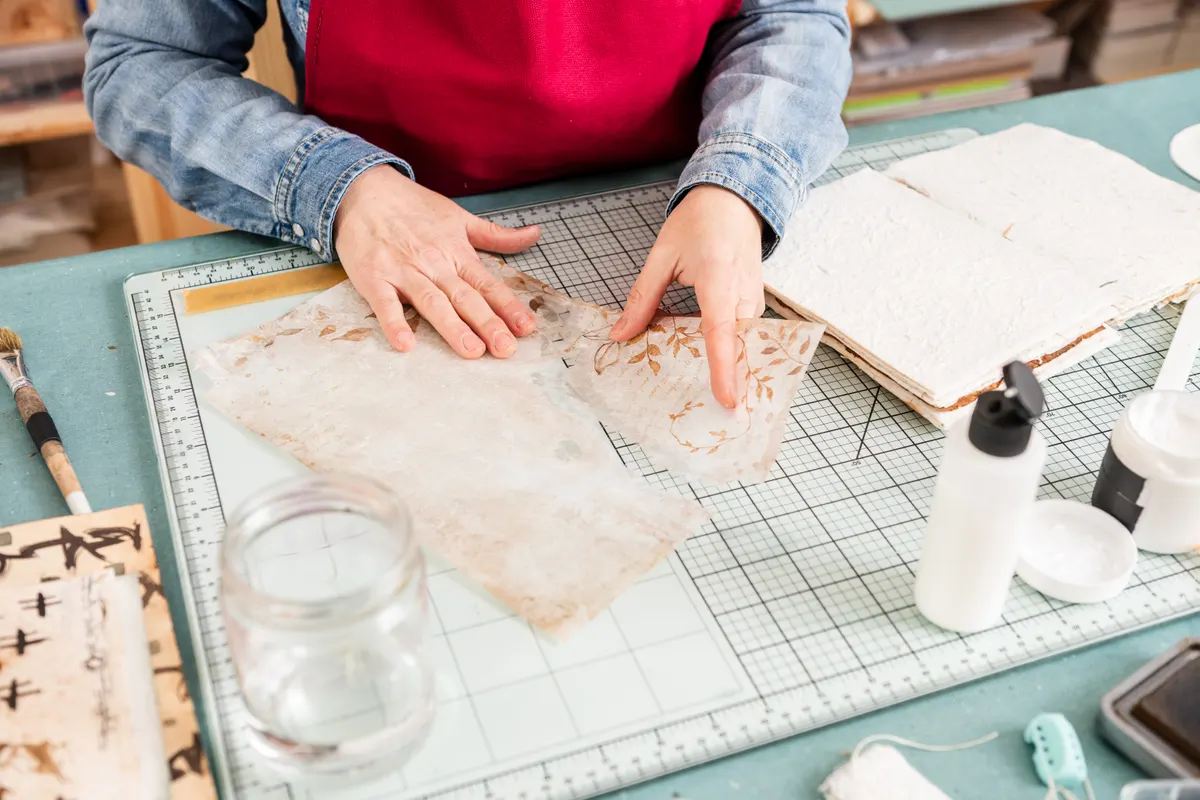 Scrapbooking supply marketing agency: woman Engages in Scrapbook Activity With Paper on Desk During Daytime at a Crafting Space.