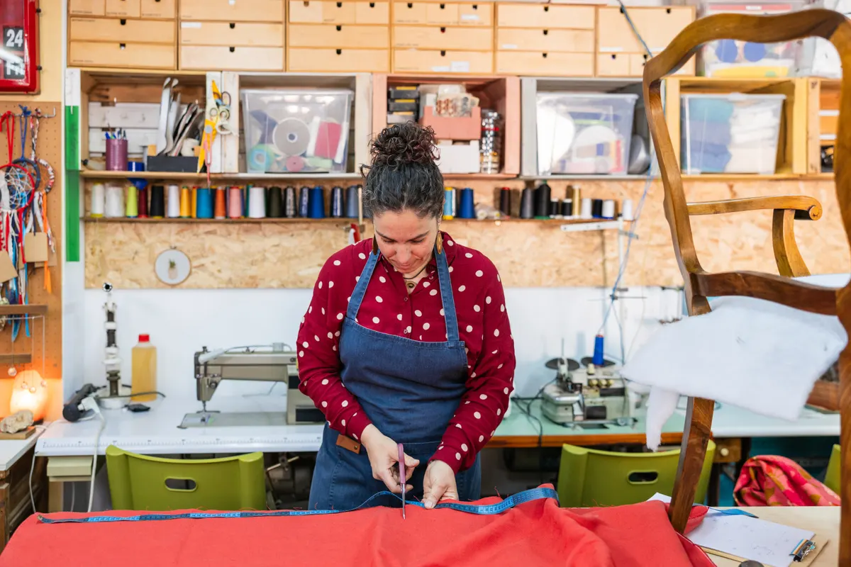 Sewing & fabric marketing agency: woman cutting red fabric for upholstery in workshop.