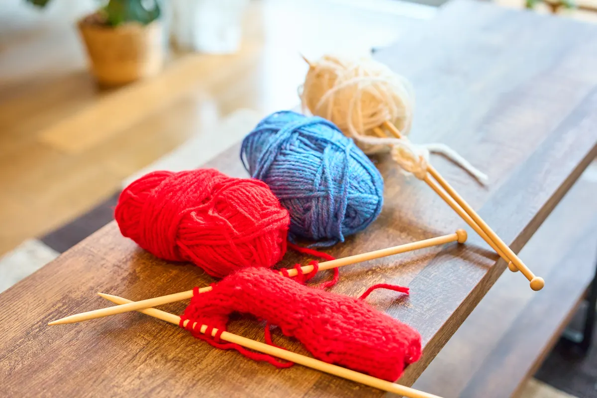 Yarn & knitting marketing agency: colorful yarn balls and knitting needles on wooden table.