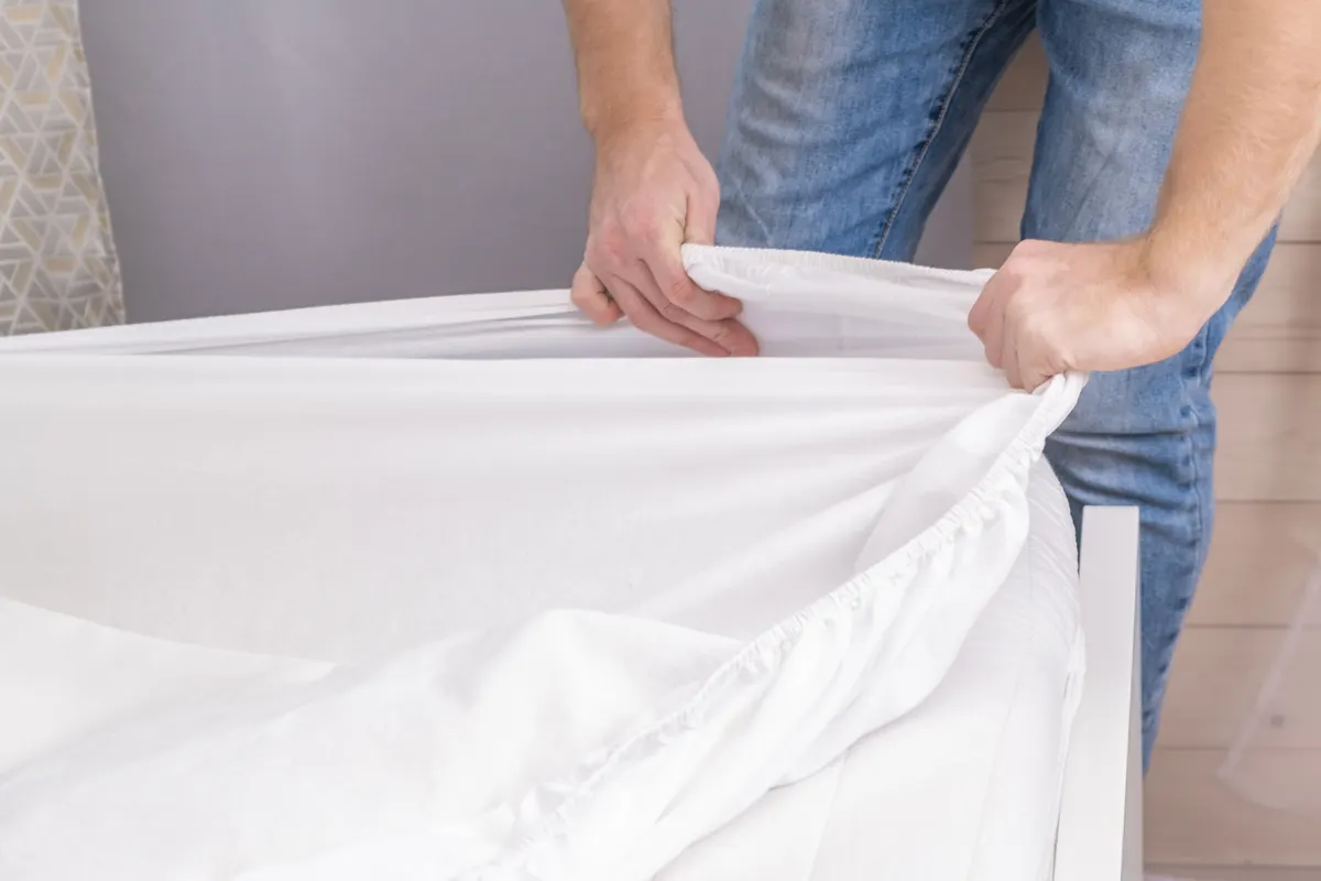 Bedding & linen marketing agency: a man makes his cozy bed with fresh bright white bed linen. Making the bed with fresh bed linen by white man. The day of the change of bedclothes. The day of washing bedclothes in the laundry room.