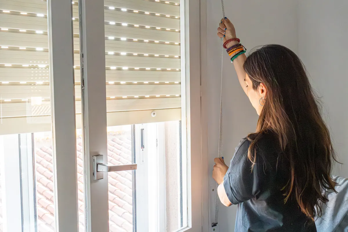 Curtain & blind marketing agency: woman adjusting roller blind on window, controlling light and privacy in a domestic setting.