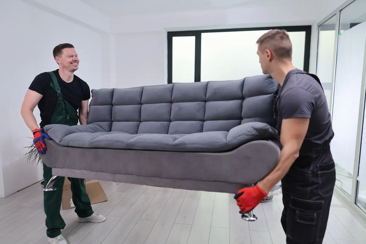 Furniture marketing agency: two friends lift a stylish gray couch in a bright room filled with excitement and effort during a weekend furniture move.