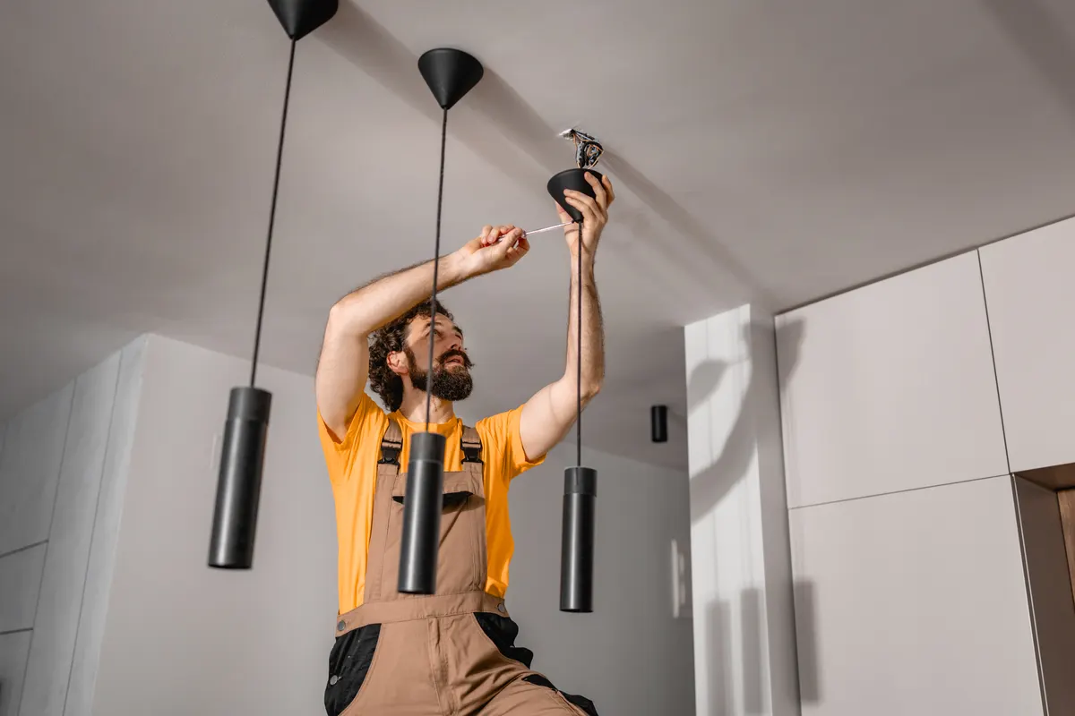 Lighting marketing agency: man installing modern pendant light fixture on ceiling during home lighting installation and repair.