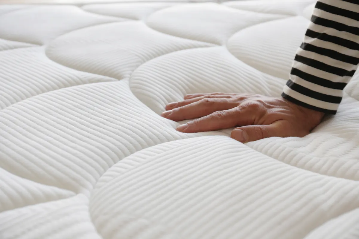 Mattress marketing agency: cropped shot of man testing white orthopedic matress on firmness.