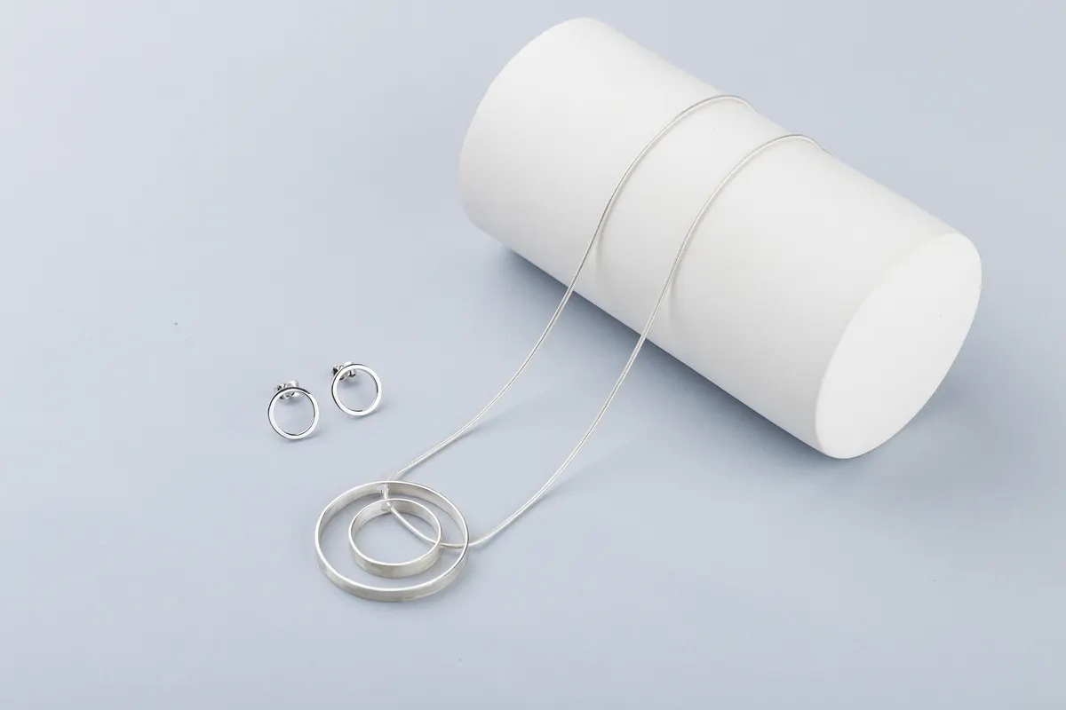 Body jewelry marketing agency: minimalist geometric silver necklace and circle stud earrings on gray background.