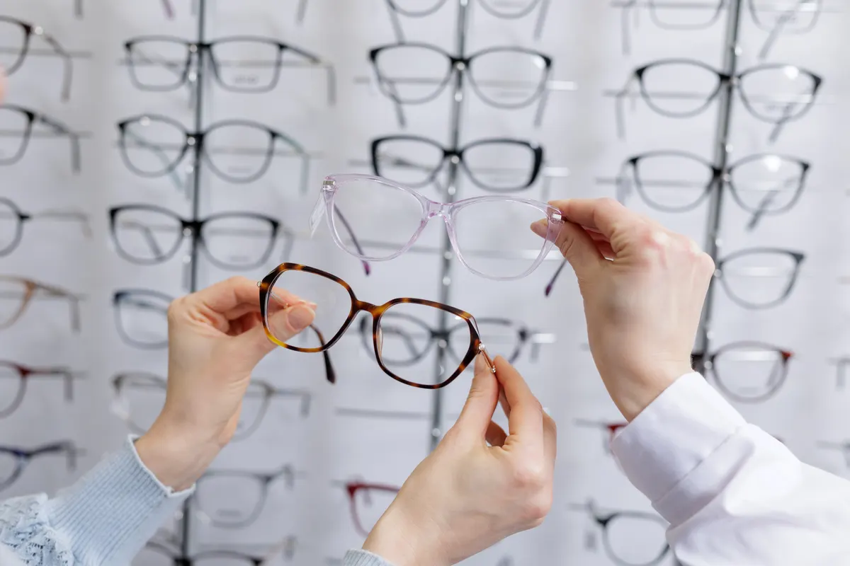 Eyewear marketing agency: hands comparing two eyeglass frames at optician store choosing best eyewear option.