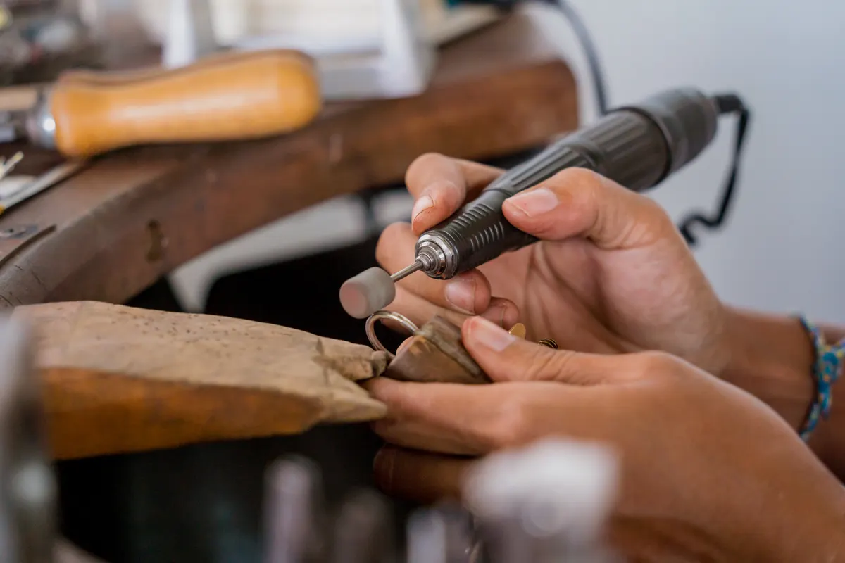 Personalized jewelry marketing agency: young faemale jeweler polishing jewelry in workshop.