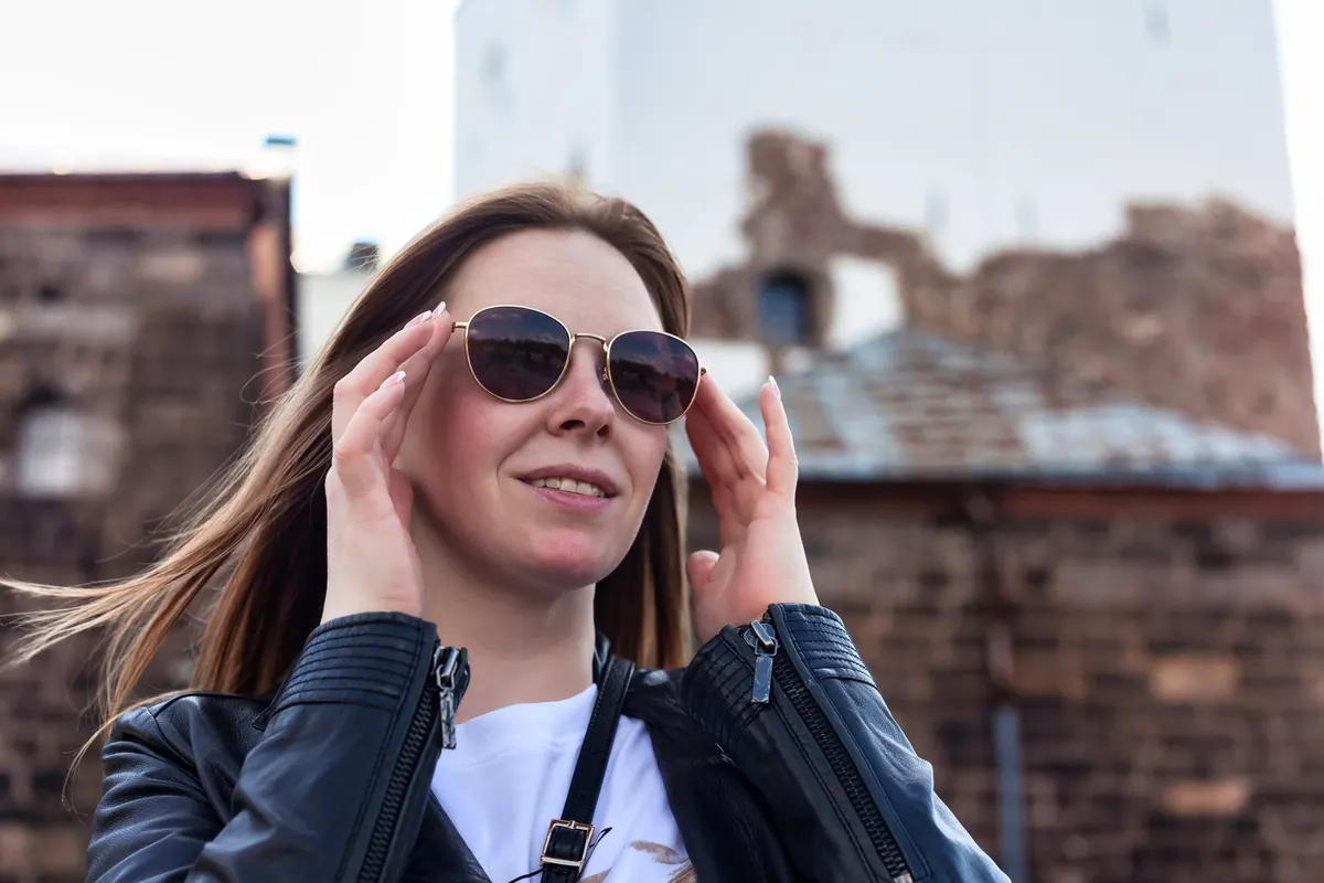 Sunglasses marketing agency: woman Enjoying a Sunny Day Outdoors While Adjusting Her Sunglasses at a Historic Location.