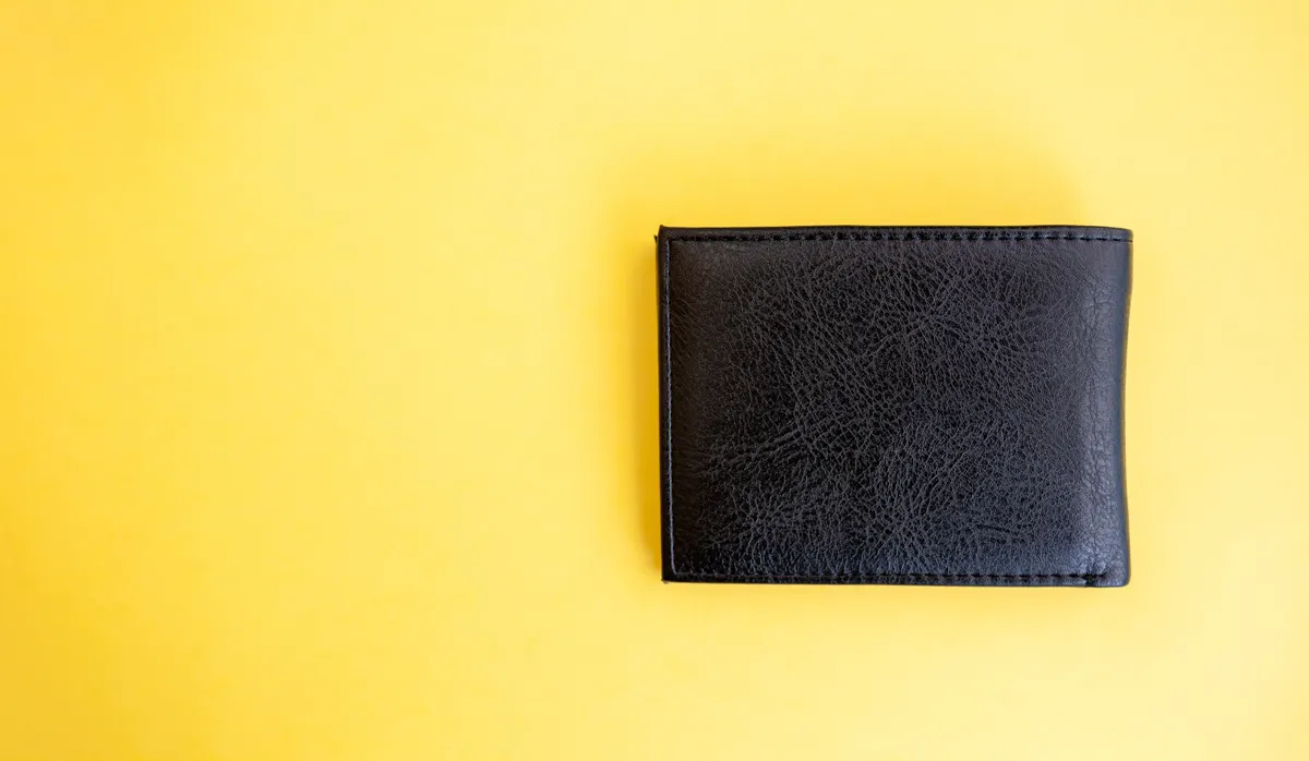 Wallet & leather goods marketing agency: black leather wallet placed on a bright yellow background, showcasing its texture and design details for product display or marketing purposes.