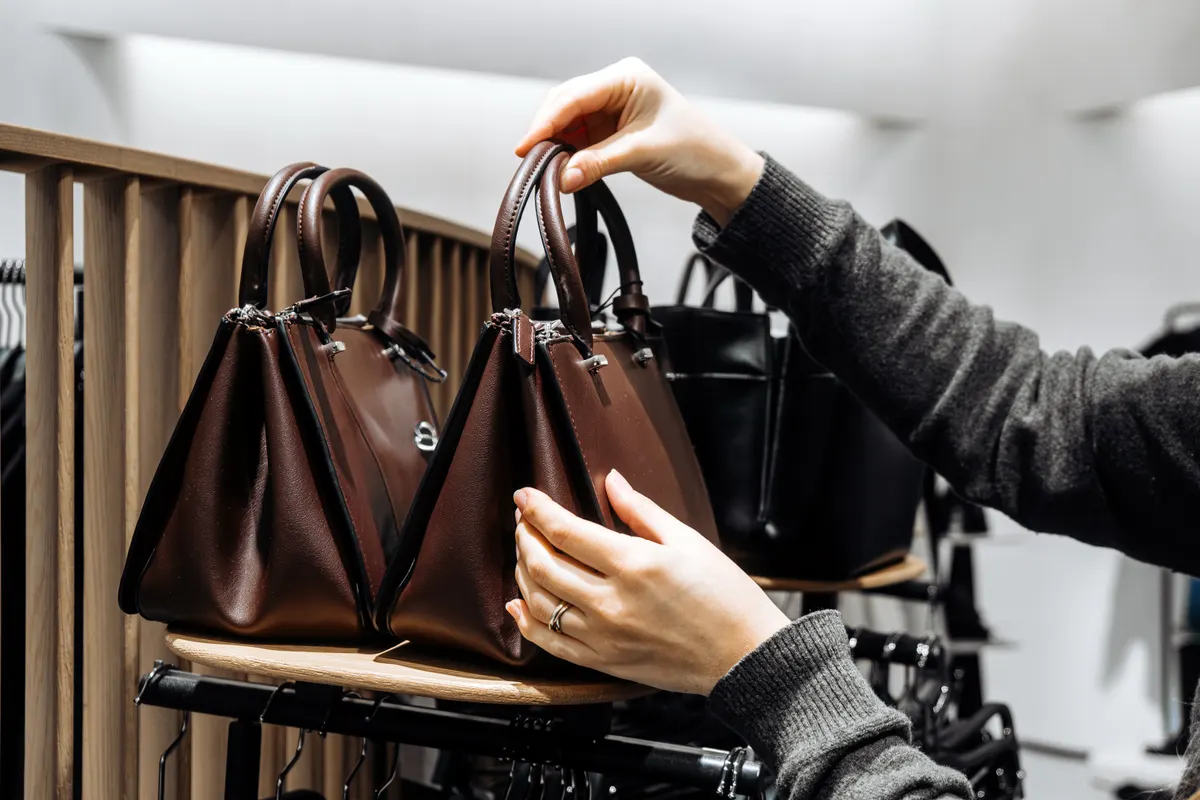 Designer handbag resale marketing agency: female shopper examining brown leather handbag on display rack.