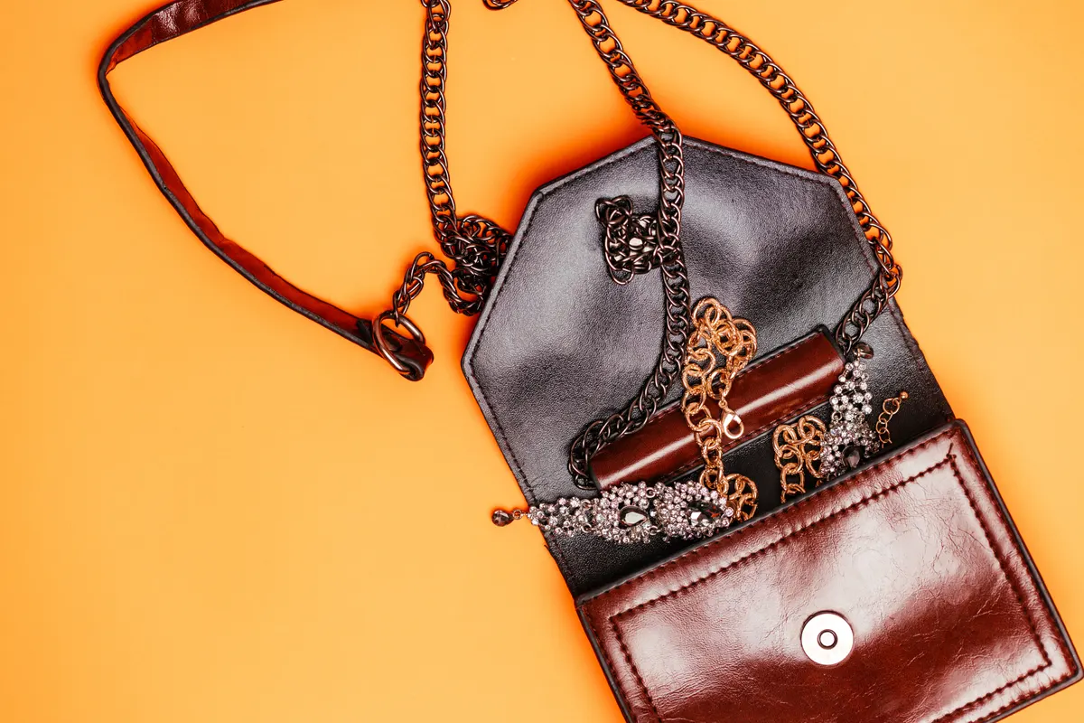 Luxury resale marketing agency: brown leather handbag with gold chain strap and jewelry accessories displayed on a vibrant orange background, showcasing an elegant fashion accessory arrangement.