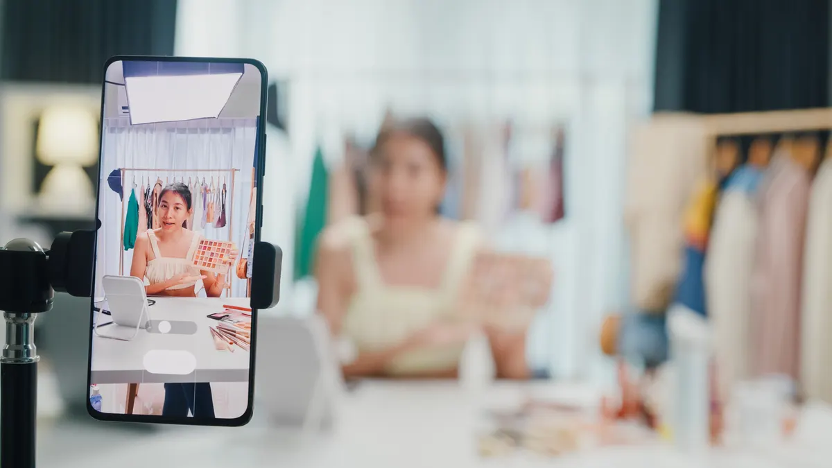 TikTok Shop marketing agency: close-up phone screen record Asia lady vlogger look phone camera review new product eye shadow palette live selling online in IG story reel tiktok work at home studio. Business online media.