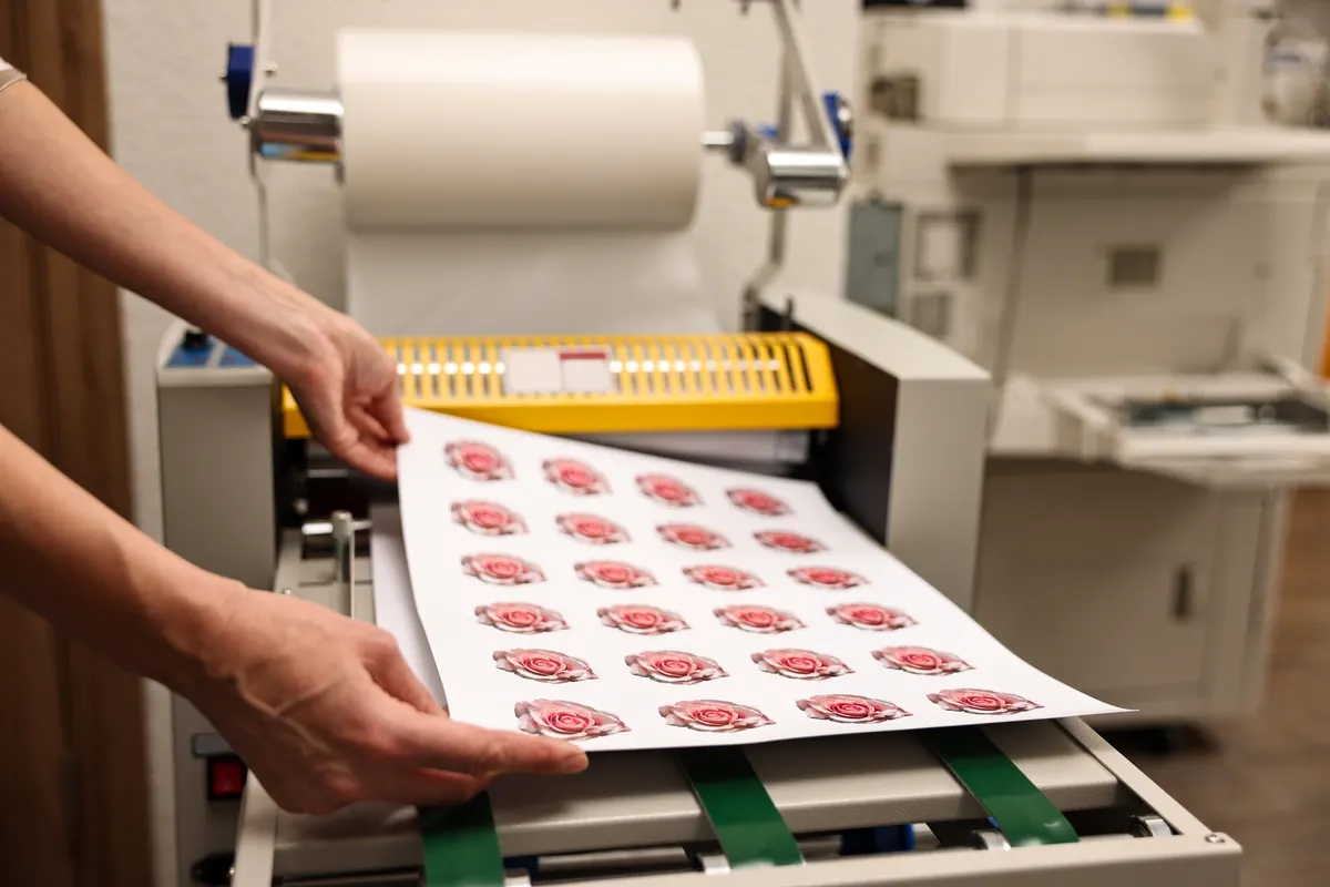 Sticker & label marketing agency: woman with printed flower stickers indoors, closeup. Printing house.