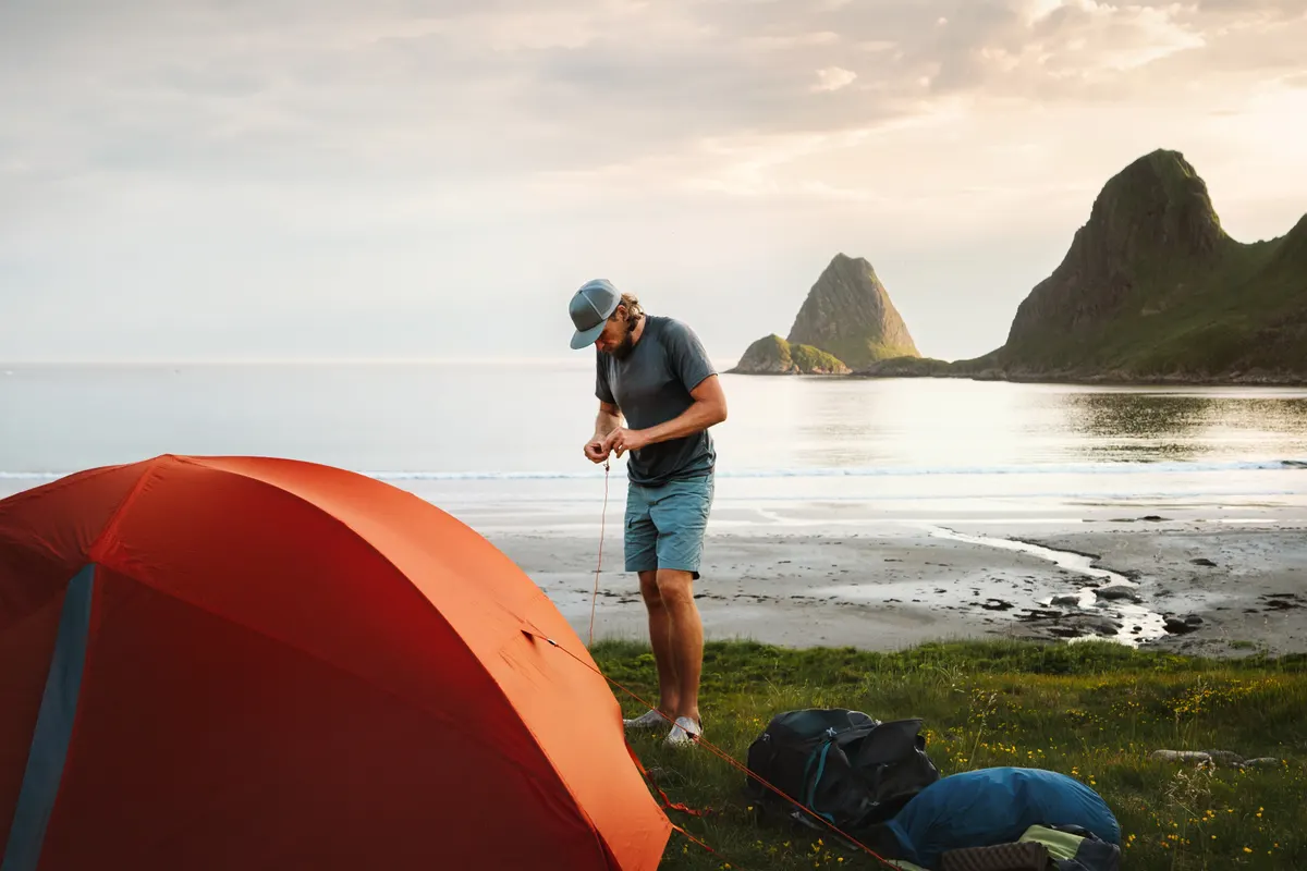 Camping & hiking gear marketing agency: man traveler setting up tent camping gear on the wild beach travel in Norway hiking adventure trip, active healthy lifestyle summer vacations with survival equipment in the great outdoors.
