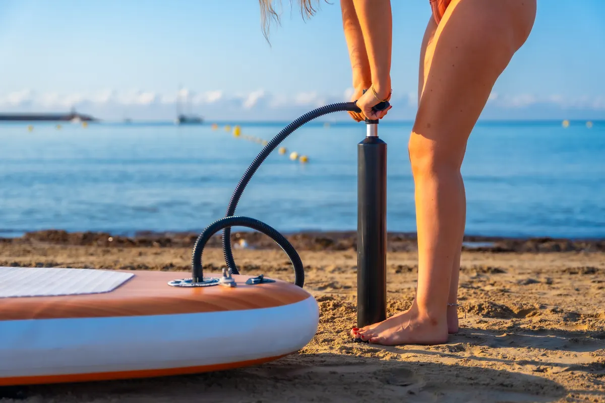 Paddleboard & kayak marketing agency: woman inflating paddle board on the beach for summer activity.