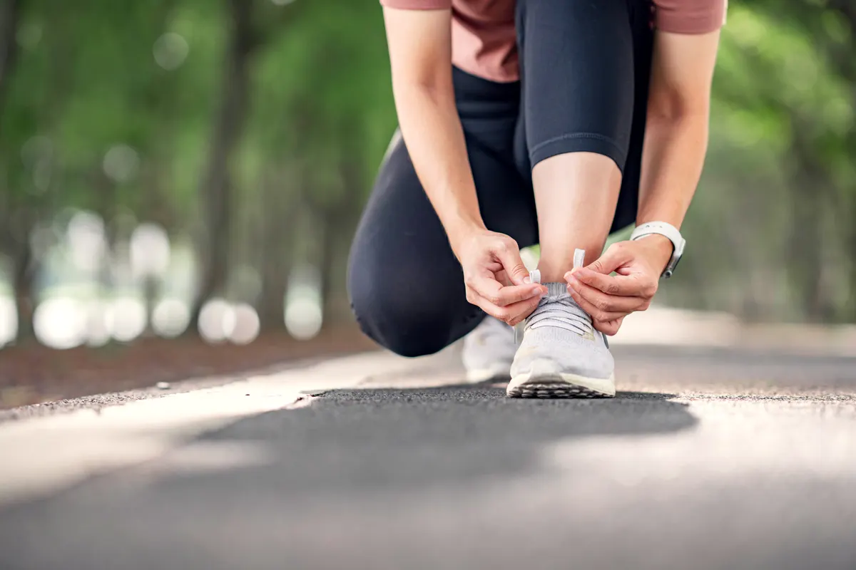 Running gear marketing agency: running shoes runner woman tying laces for summer run in forest park. Jogging girl exercise motivation heatlh and fitness exercise. copy space.