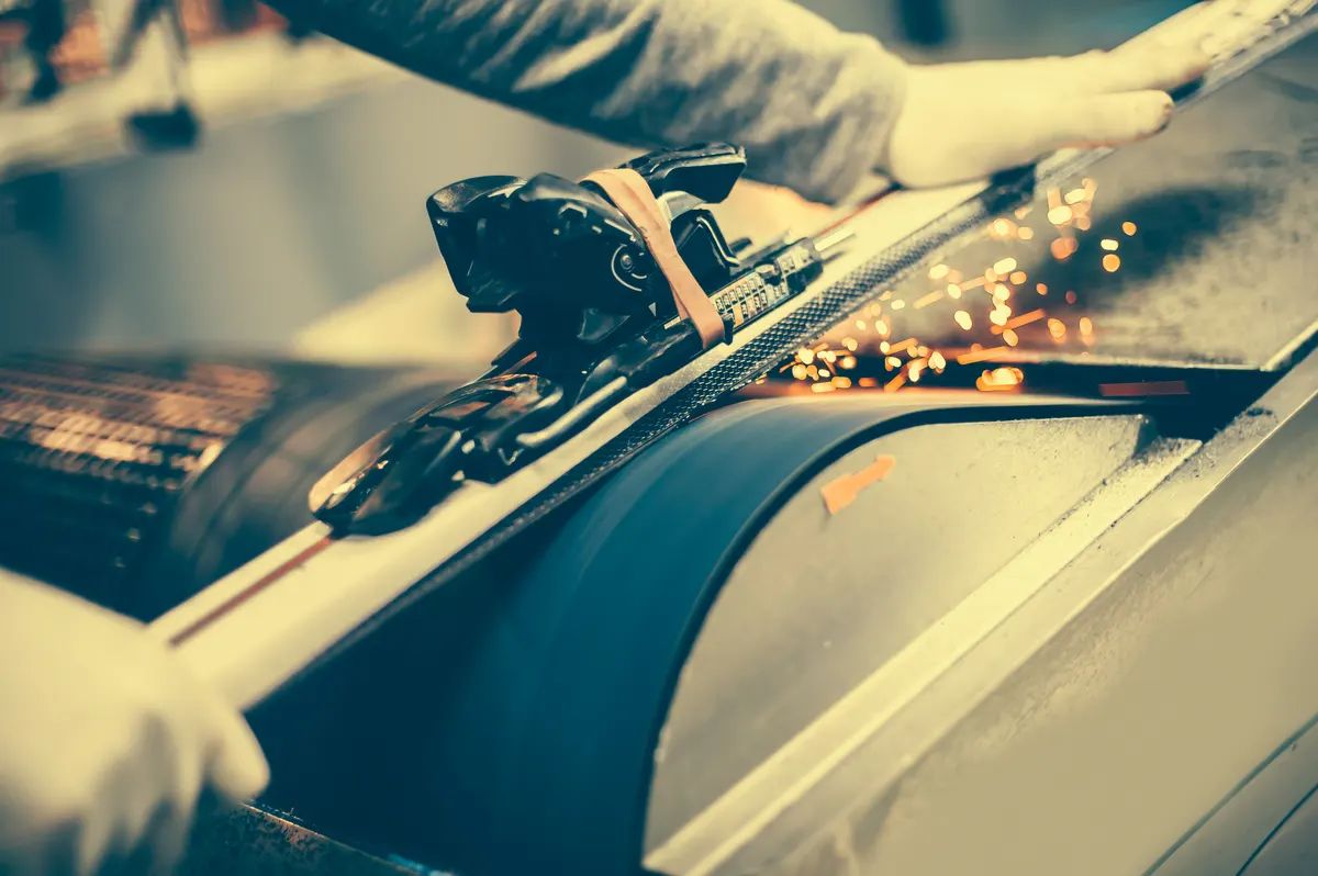 Ski & snowboard marketing agency: ski tuning and reapairs. Winter shop worker doing base repair.