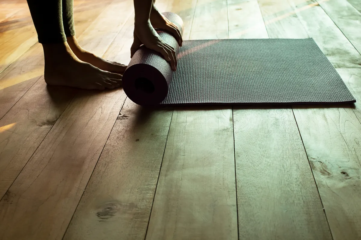 Yoga product marketing agency: hands and foot of woman wearing grey sporty pants rolling fitness mat before, after class in yoga studio club or at home on wooden floor sport healthy lifestyle concept.