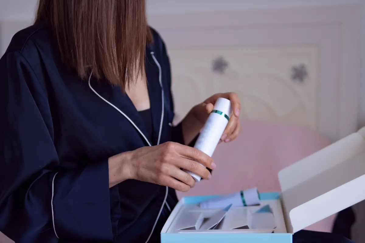 Beauty subscription marketing agency: woman unboxing a beauty product subscription box, holding a skincare serum bottle, enjoying a relaxed morning routine at home.