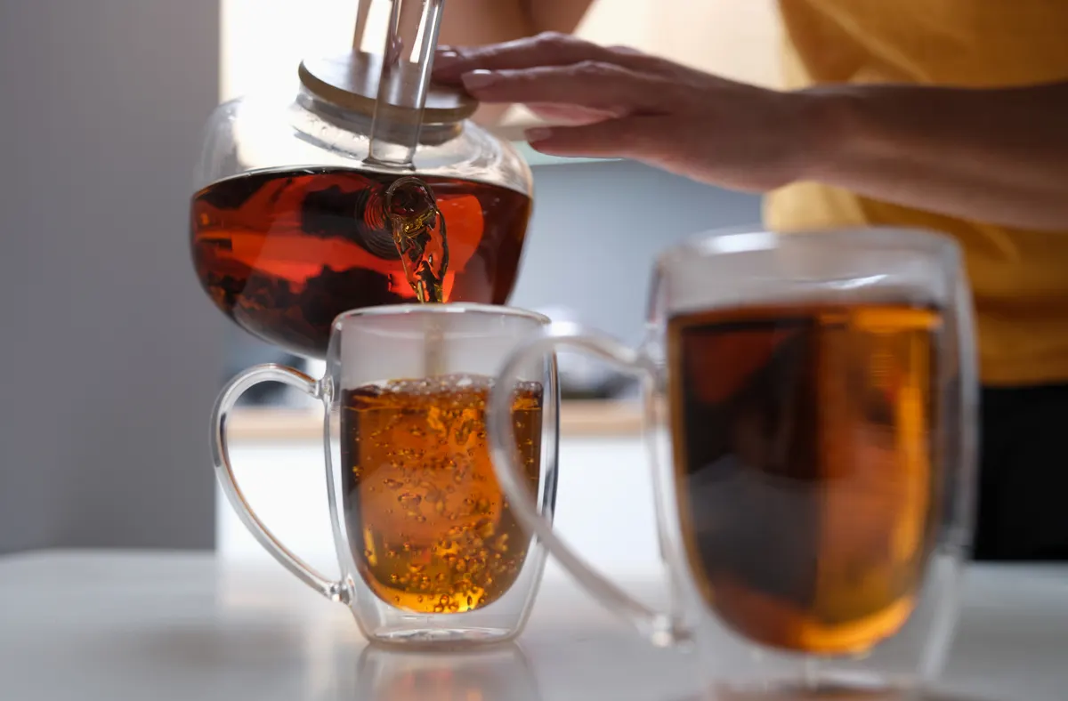 Tea subscription marketing agency: woman pouring black tea from teapot into cup closeup.