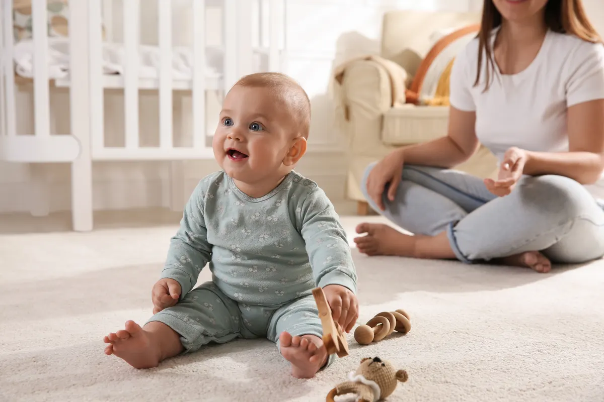 Baby toy marketing agency: cute baby girl playing with wooden toys and mother on floor at home.