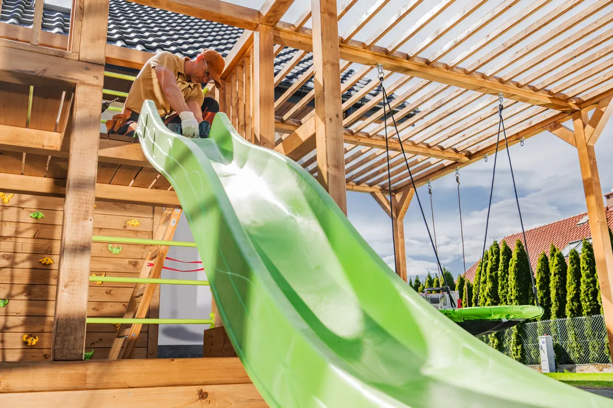 Outdoor play equipment marketing agency: construction of a Vibrant Green Slide on a Wooden Play Structure in a Backyard During Sunny Weather With Partially Cloudy Skies.