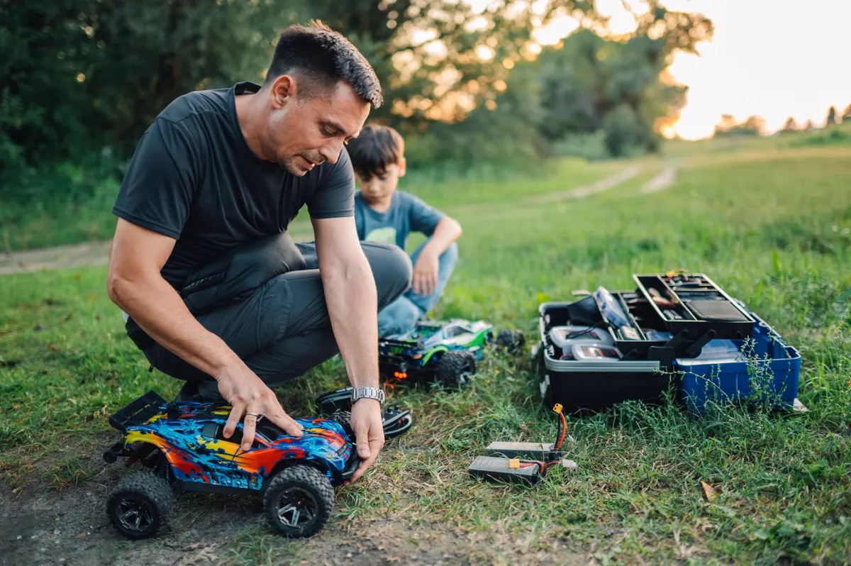 Remote-control toy marketing agency: father and his son fixing toy cars and replacing batteries in nature.