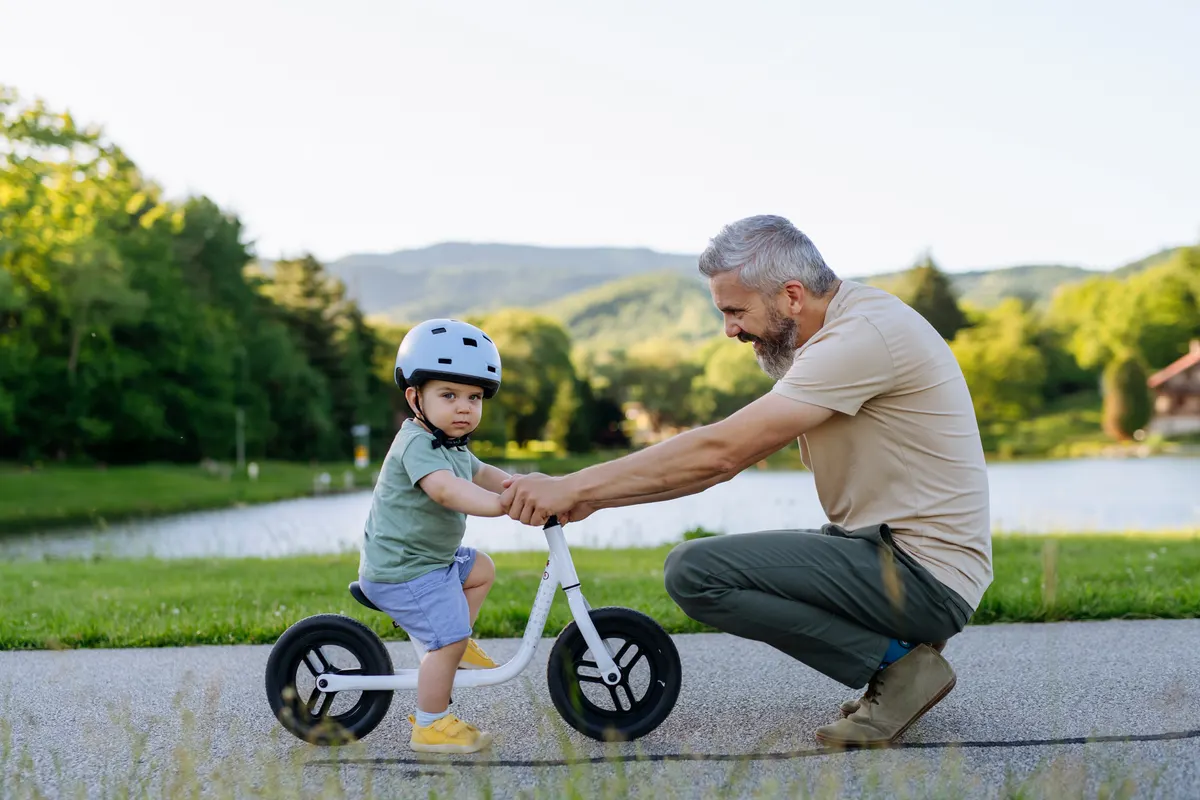 Ride-on toy marketing agency: father helping toddler son learn to ride balance bike for the first time.