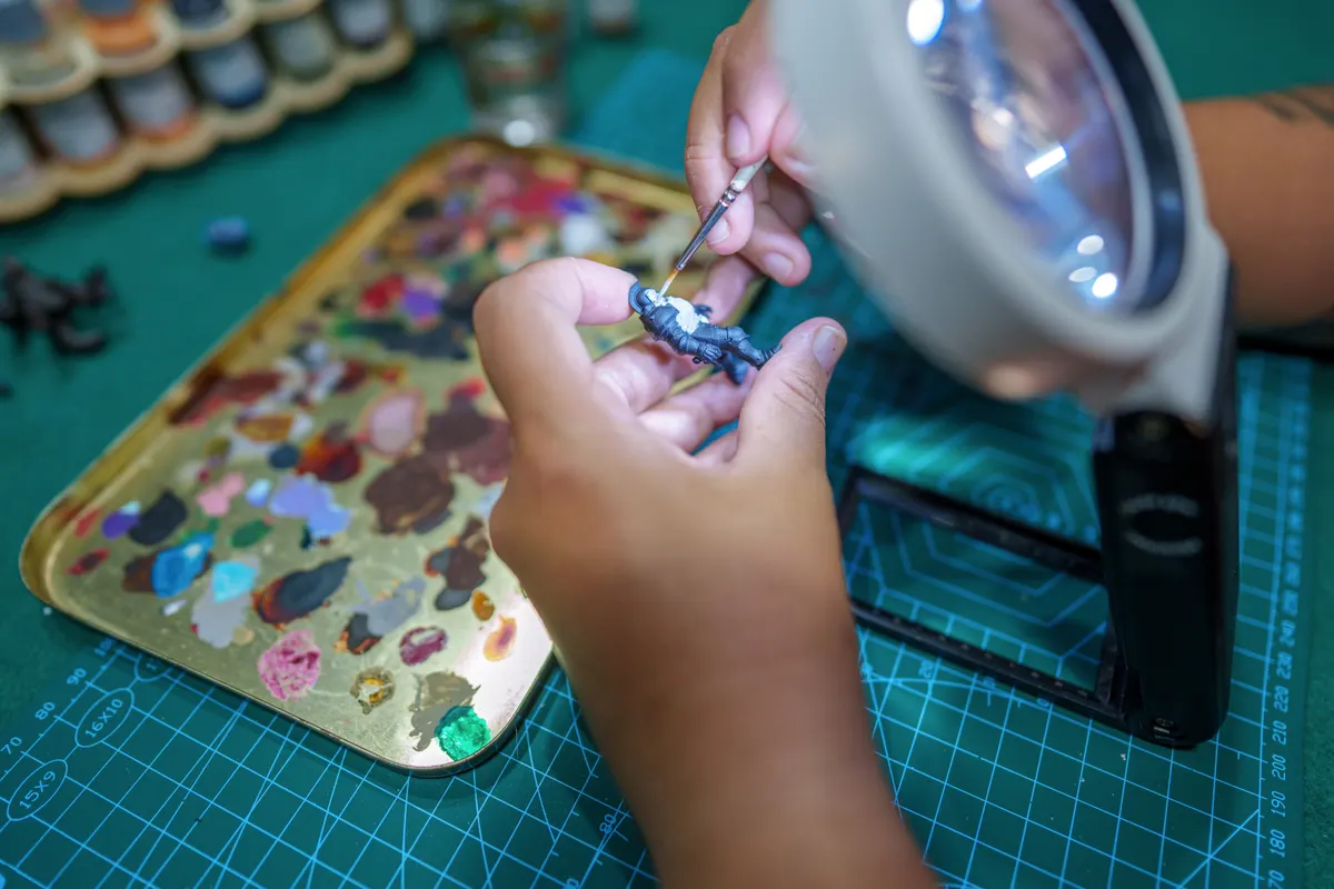 Tabletop miniature marketing agency: woman painting miniature figurine with magnifying glass.