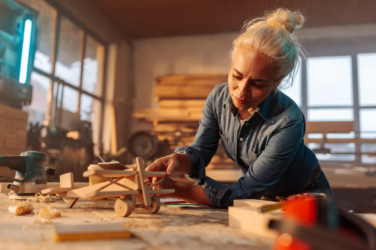 Wooden toy marketing agency: carpenter crafting wooden toy airplane in workshop.