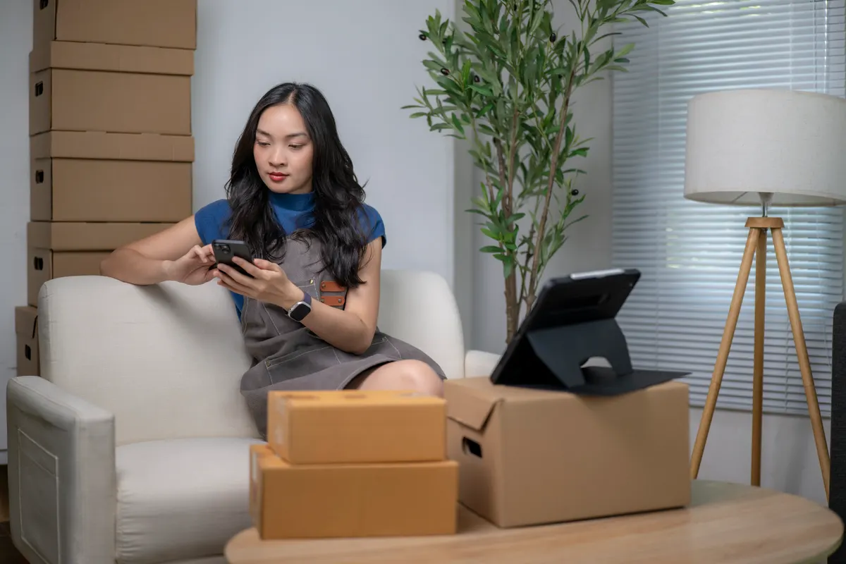 A store owner at a laptop with a stack of boxes ready to ship