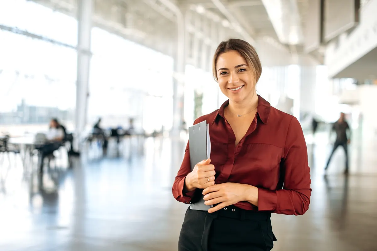 Google Merchant Center management: portrait of a successful gorgeous stylish elegant caucasian business lady, hr or product manager, standing in coworking center, holding documents, looking at the camera, smiling friendly.